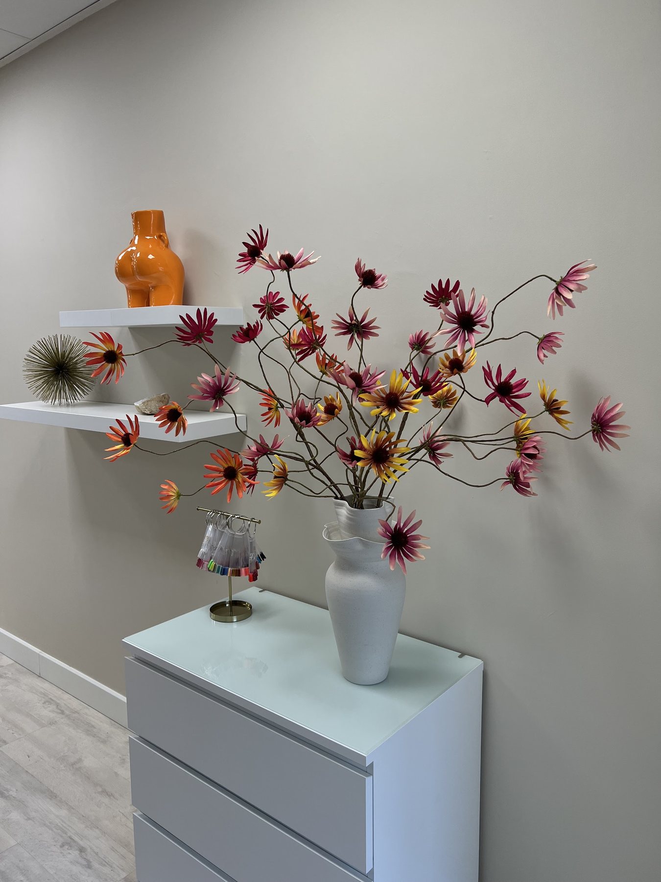 Een hoek van de salon met wandplanken, bloemen en een oranje vaas