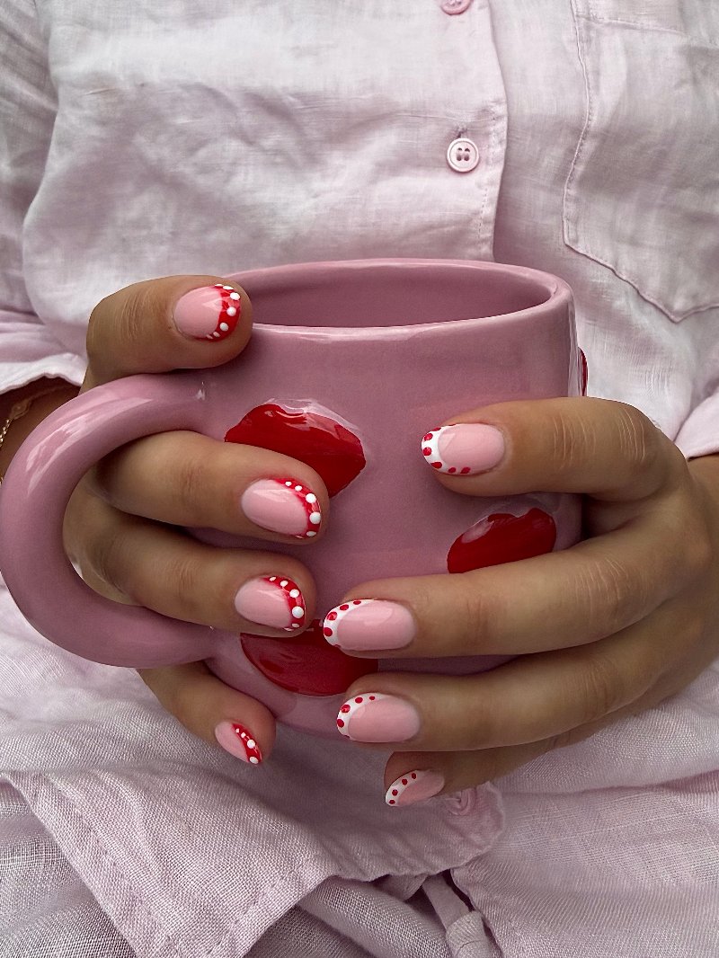 Roze nagels met rode stipjes rond een roze mok